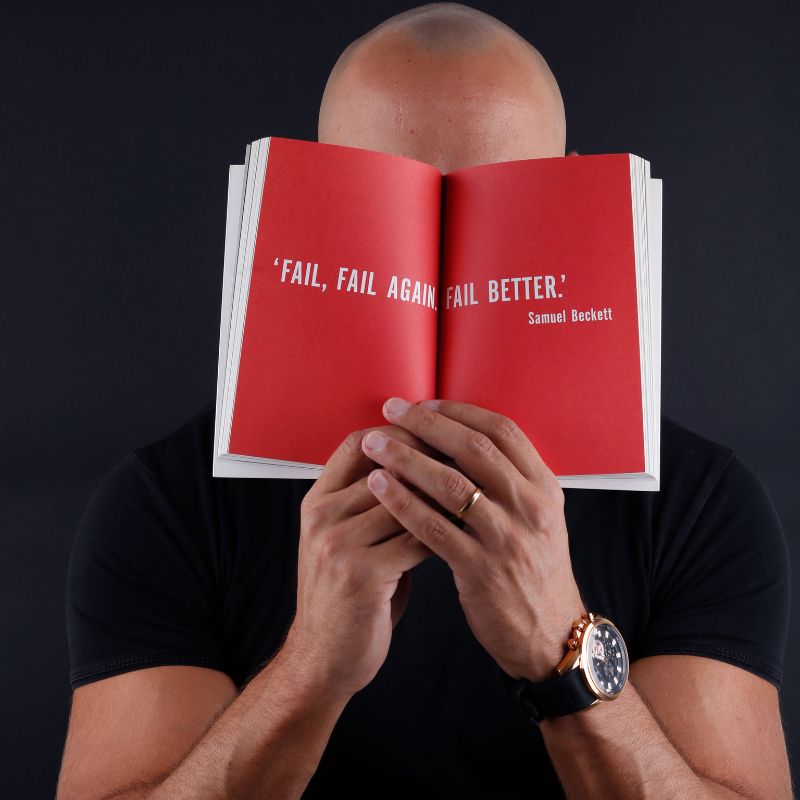 A man with a book in his face that says: "Fail, Fail Again, Fail Better"