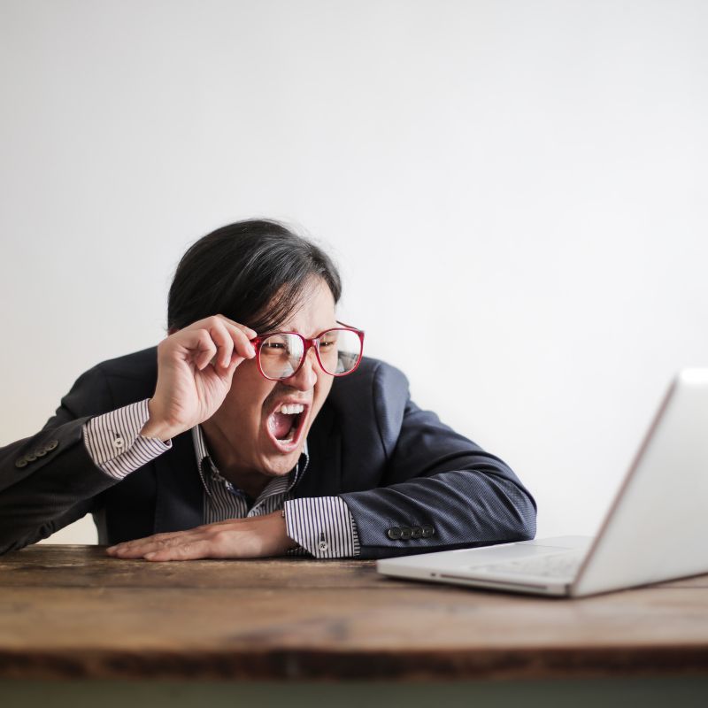 A man shouting in front of the computer and pushing up his glasses